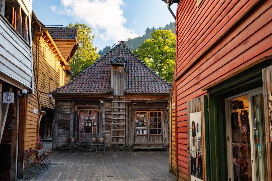An outdoor scene at Bryggen in Bergen featuring a row of colorful historic wooden buildings with gabled roofs in shades of yellow, red, and white, some with visible signage such as 'O'Connor's' and 'S